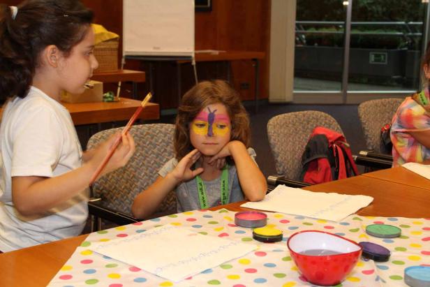 Ein Mädchen bemalt das Gesicht eines anderen Mädchens mit einem Schmetterling.
