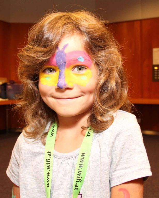 Ein Mädchen mit Gesichtsbemalung in Form eines Schmetterlings lächelt.