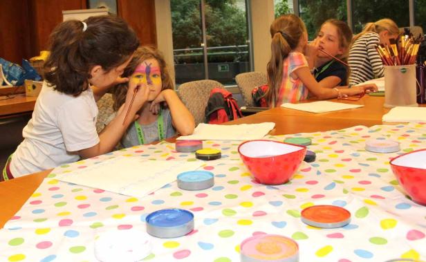 Ein Mädchen bekommt mit einem Pinsel eine bunte Schmetterlingsbemalung auf ihr Gesicht.