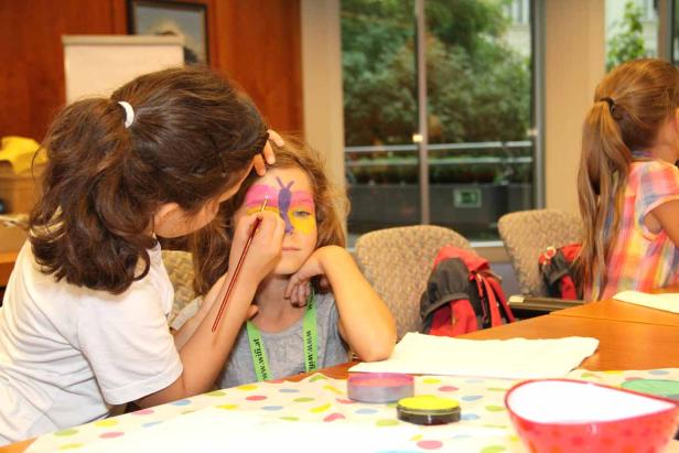 Ein Mädchen bekommt ein Schmetterlingsgesicht von einem anderen Mädchen geschminkt.