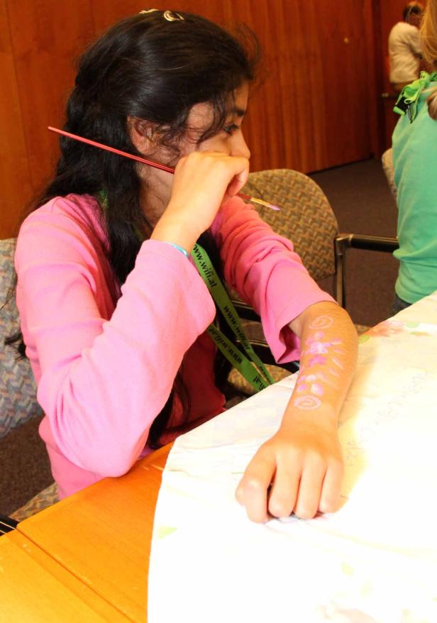 Ein Mädchen bemalt ihren Arm mit einem Pinsel.