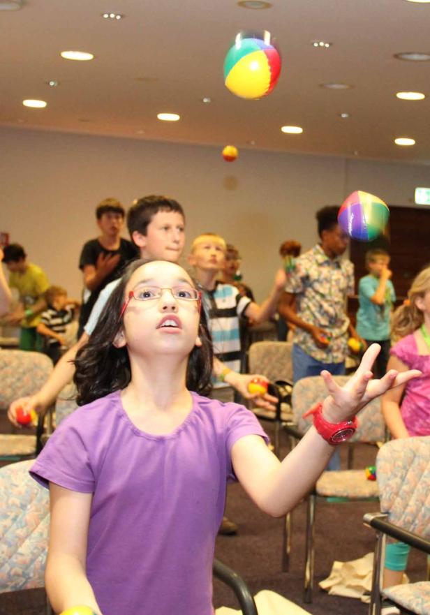 Eine Gruppe Kinder übt sich im Jonglieren mit bunten Bällen.