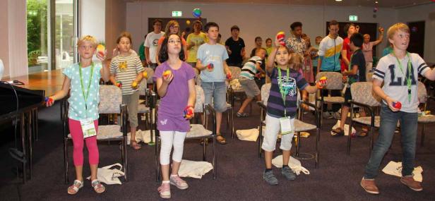 Eine Gruppe Kinder übt das Jonglieren mit bunten Bällen in einem Raum.