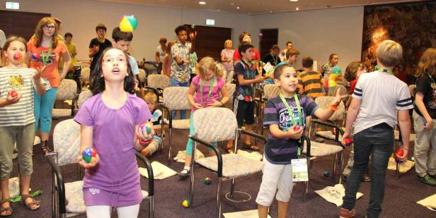 Eine Gruppe Kinder übt sich im Jonglieren mit bunten Bällen in einem Raum.