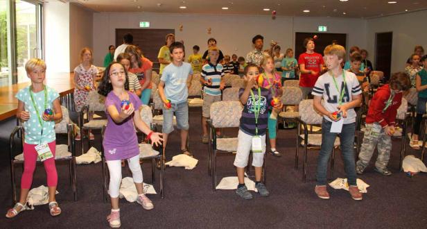 Eine Gruppe Kinder übt sich im Jonglieren mit bunten Bällen in einem Raum.