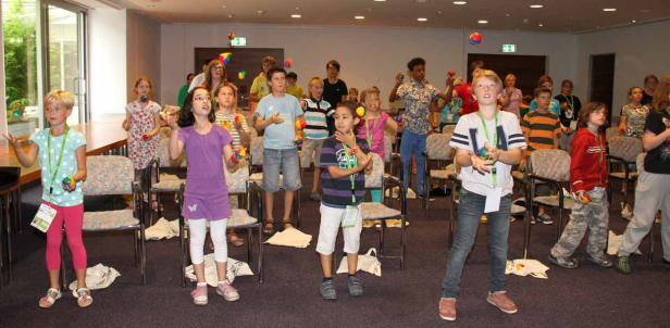 Eine Gruppe Kinder übt das Jonglieren mit bunten Bällen in einem Raum.