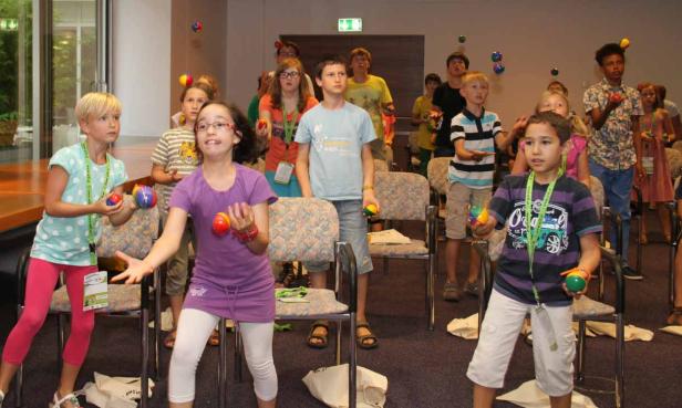 Eine Gruppe Kinder übt sich im Jonglieren mit bunten Bällen in einem Raum.