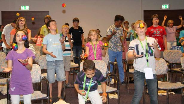 Eine Gruppe von Kindern übt das Jonglieren mit bunten Bällen in einem Raum.