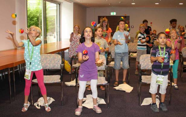 Eine Gruppe Kinder übt sich im Jonglieren mit bunten Bällen in einem Raum.