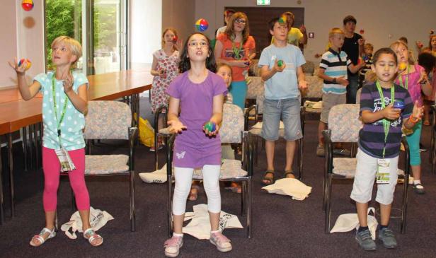 Eine Gruppe Kinder übt das Jonglieren mit bunten Bällen in einem Raum.