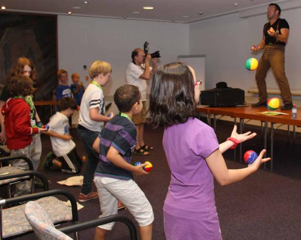 Eine Gruppe Kinder lernt von einem Mann, wie man mit Bällen jongliert.