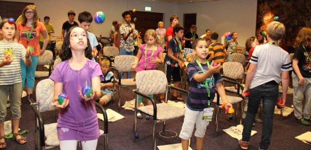 Eine Gruppe von Kindern übt Jonglieren mit bunten Bällen in einem Raum.