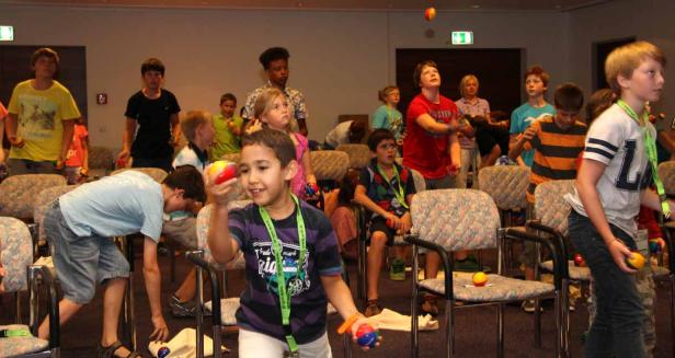 Eine Gruppe von Kindern übt das Jonglieren mit bunten Bällen in einem Raum.