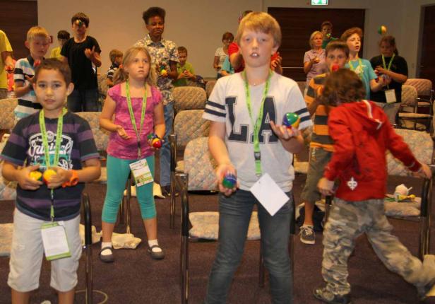 Eine Gruppe Kinder übt Jonglieren mit bunten Bällen in einem Raum.