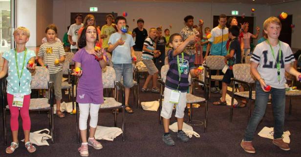 Eine Gruppe von Kindern übt das Jonglieren mit bunten Bällen in einem Raum.