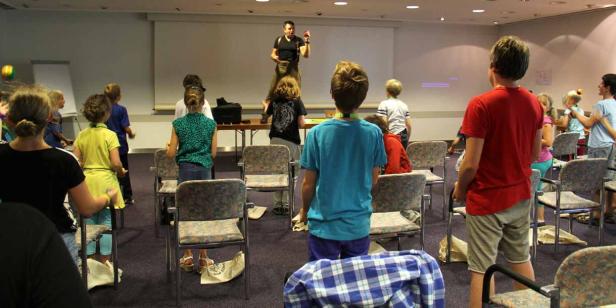 Ein Mann auf einem Tisch jongliert vor einer Gruppe von Kindern.