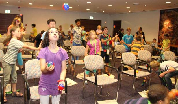 Eine Gruppe Kinder übt in einem Raum das Jonglieren mit bunten Bällen.