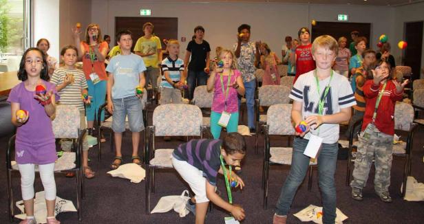 Eine Gruppe von Kindern übt das Jonglieren mit kleinen Bällen in einem Raum.