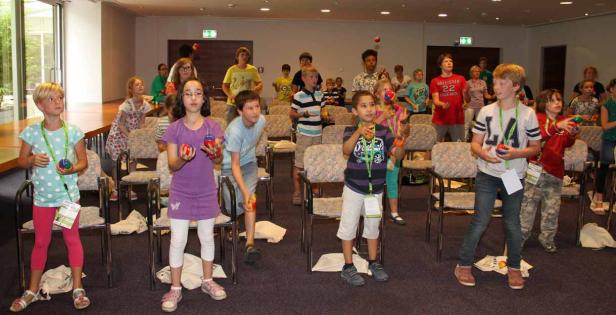 Eine Gruppe Kinder übt in einem Raum das Jonglieren mit Bällen.