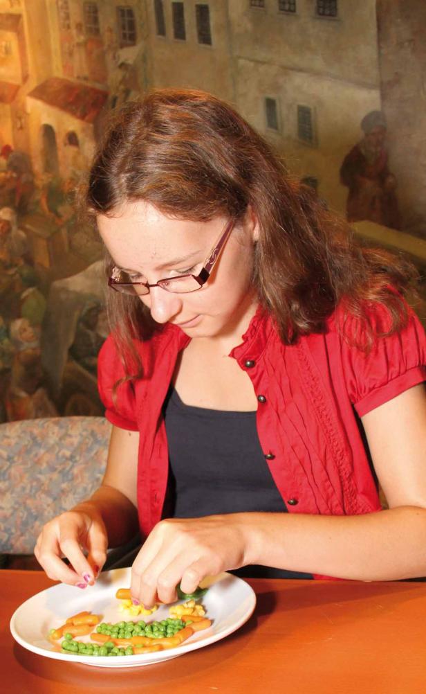 Eine junge Frau mit Brille ordnet Gemüse auf einem Teller an.