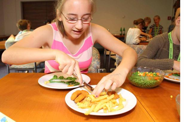 Ein Mädchen isst Erbsen und Pommes Frites mit einem Messer.