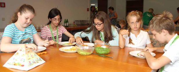 Eine Gruppe Kinder sitzt an einem Tisch und isst Gemüse und Pommes Frites.