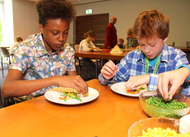 Zwei Kinder legen Gemüse auf ihre Teller.