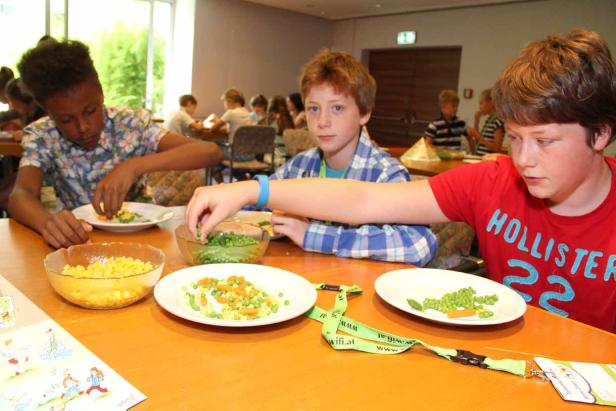 Drei Kinder sitzen an einem Tisch und bereiten eine Mahlzeit mit Gemüse zu.