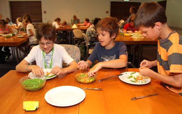 Kinder sitzen an Tischen und bereiten Mahlzeiten mit Gemüse zu.