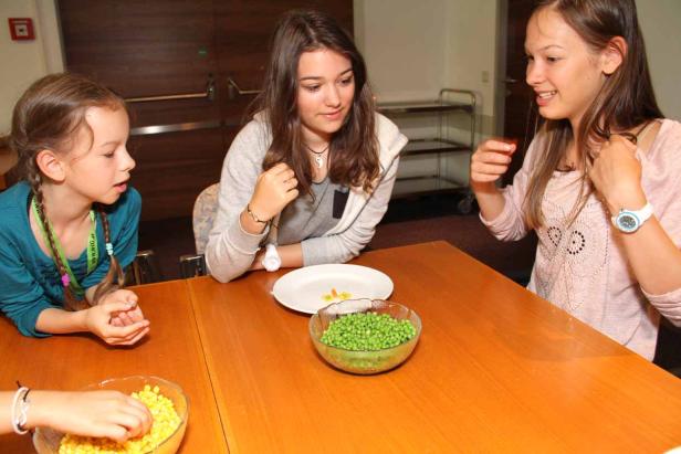 Drei Mädchen sitzen an einem Tisch mit Schüsseln mit Erbsen und Mais.