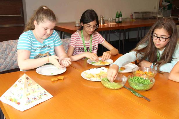 Drei Mädchen sitzen an einem Tisch und bereiten eine Mahlzeit mit Gemüse und Nuggets zu.