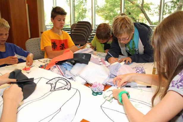Eine Gruppe Kinder bastelt an einem Tisch mit Stoffresten und Papier.