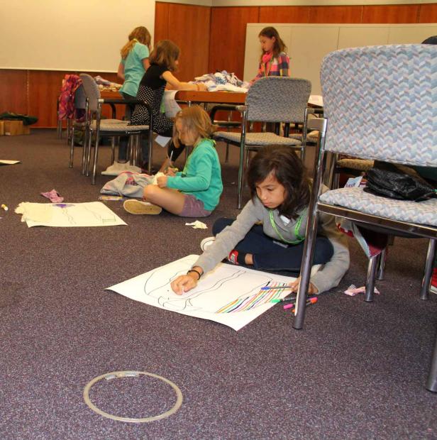 Mehrere Mädchen sitzen auf dem Boden und an einem Tisch und malen und basteln.