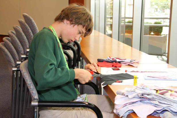 Ein junger Mann schneidet Stoff an einem Tisch mit Stoffresten.