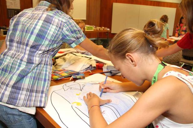 Ein Mädchen bemalt ein Hemd auf einem großen Papierbogen.