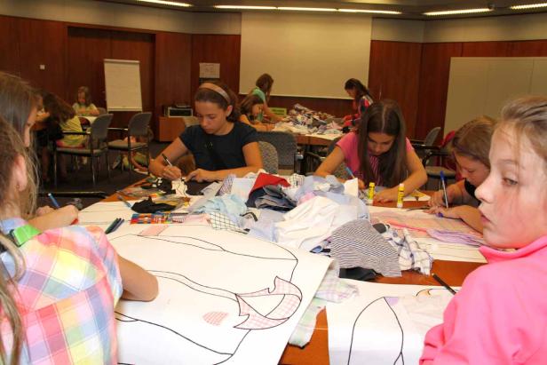 Eine Gruppe Mädchen arbeitet an einem Tisch mit Stoffresten und Papierzeichnungen.