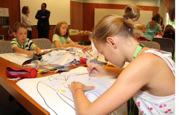 Kinder bemalen Hemden auf Papier in einem hellen Raum.