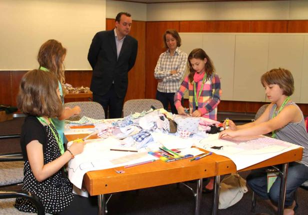 Kinder basteln an einem Tisch mit Stoffresten, während Erwachsene zusehen.