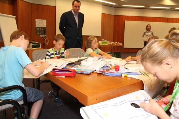Kinder sitzen an einem Tisch und basteln mit Papier und Stiften.