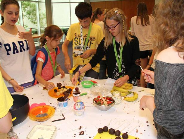 Eine Gruppe Kinder dekoriert Schokoladenkugeln mit verschiedenen Zutaten wie Erdbeeren und Bananen.