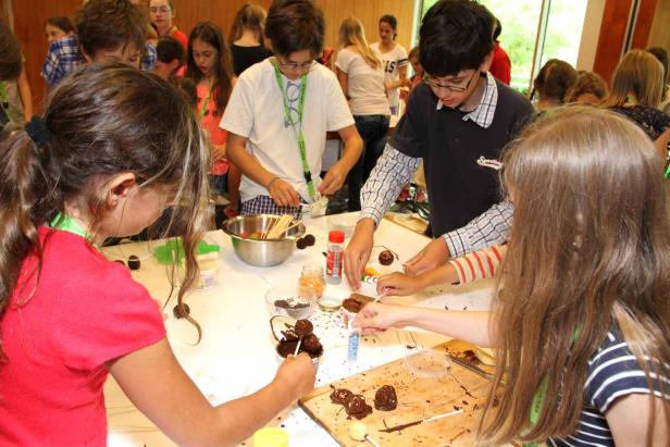 Kinder verzieren Schokoladenkugeln auf Stielen mit Streuseln.