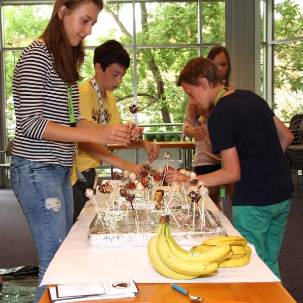 Eine Gruppe Jugendlicher dekoriert Cake Pops an einem Tisch mit Bananen.