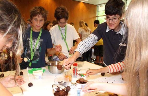 Eine Gruppe Kinder dekoriert Schokoladenkugeln mit Streuseln und anderen Zutaten.