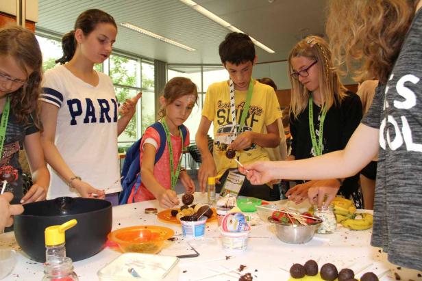 Eine Gruppe von Kindern dekoriert Cake Pops mit Schokolade und Streuseln.
