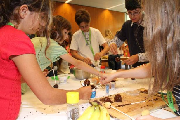 Eine Gruppe Kinder bereitet Schokoladenfrüchte am Stiel zu.