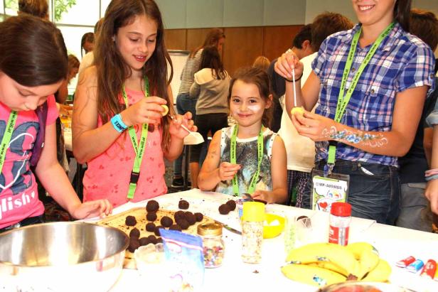 Mehrere Kinder verzieren Schokoladenkugeln mit Zuckerstreuseln und anderen Dekorationen.