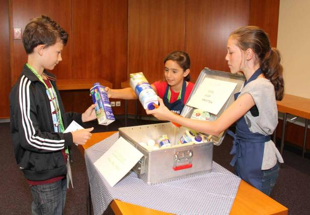 Drei Kinder sortieren Lebensmittel in einen Behälter.