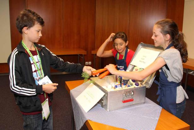 Drei Kinder hantieren mit Lebensmitteln in einer Metallkiste.