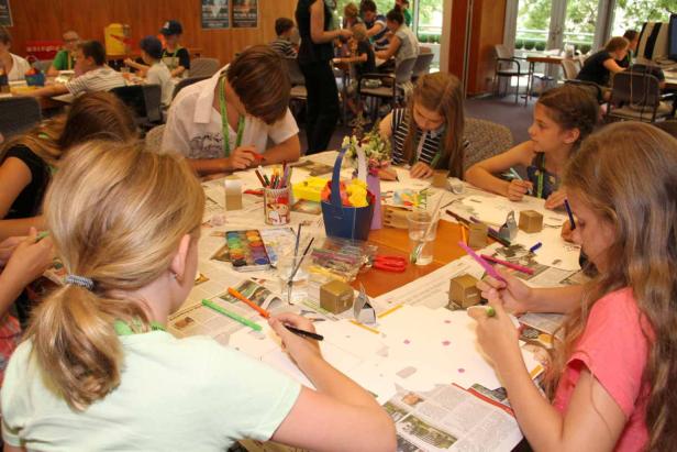 Eine Gruppe Kinder sitzt an einem Tisch und bastelt mit Stiften und Farben.