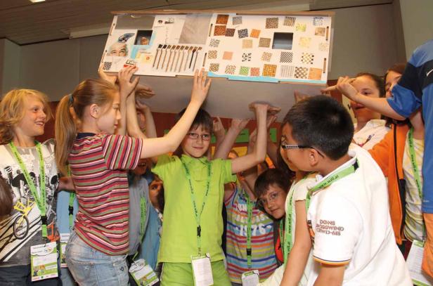 Eine Gruppe Kinder hält gemeinsam ein großes, dekoriertes Modellhaus hoch.